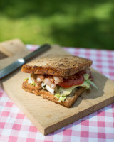 Bacon, tomato, salad sandwich on a wooden board at a picnic table