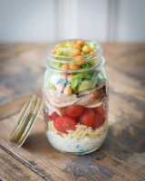 Jar with ranch dressing, orzo pasta, cherry tomatoes, chicken salad and soup pearl croutons