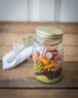Jar of ingredients for a lentil soup, such as powdered stock, lentils, carrots, peas and sausages