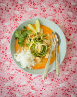 Bowl with yellow curry, chicken, cashew nuts, zucchini noodles, cilantro and lemon wedges on a pink background with white bunnies