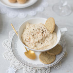 Cup of hummus dip with some oatmeal cookies with another plate of fingerfood and a glass of champagne in the background